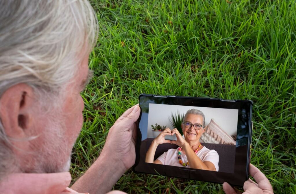An older adult sits outdoors while video chatting an online dating match.