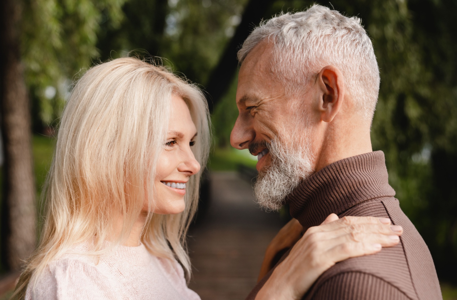 An older adult couple embrace and smile at each other.