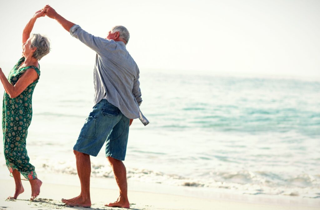 An older adult couple dance together on the beach.

