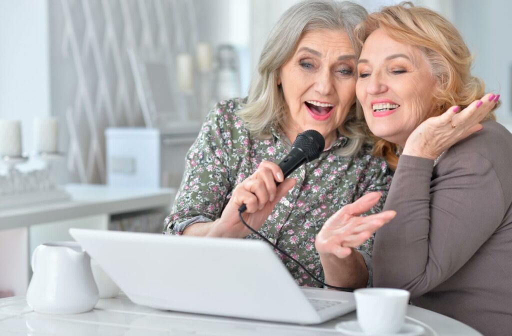 Two older adults use a microphone attached to a laptop to sing karaoke with friends over the internet.